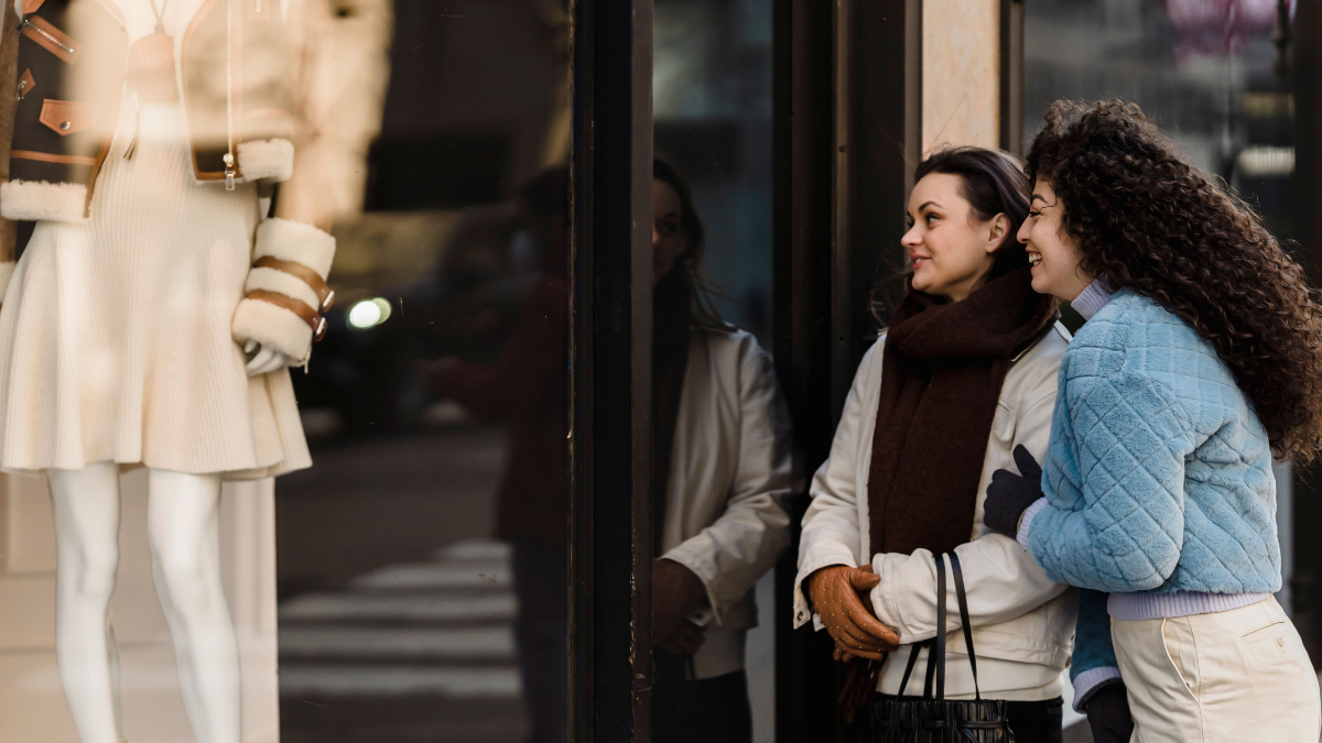 Two women enjoying window shopping in a stylish urban area, reflecting joy and friendship.